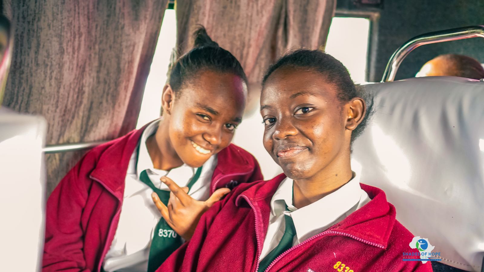 Two students smiling in their seats on the bus