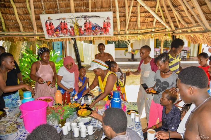The group preparing a meal together under a thatched shelter