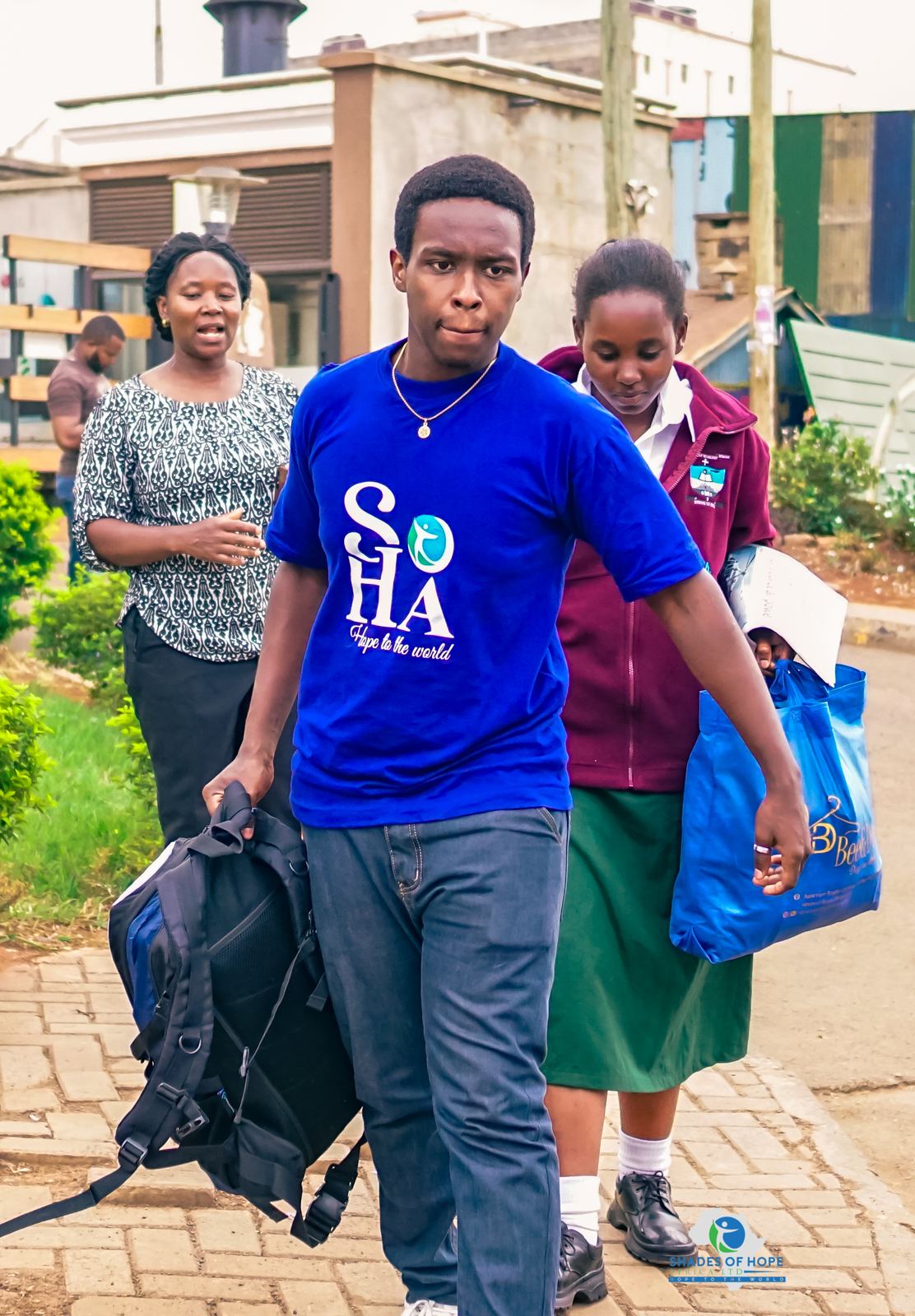 A young man in a SOHA T-shirt carrying a student's bags